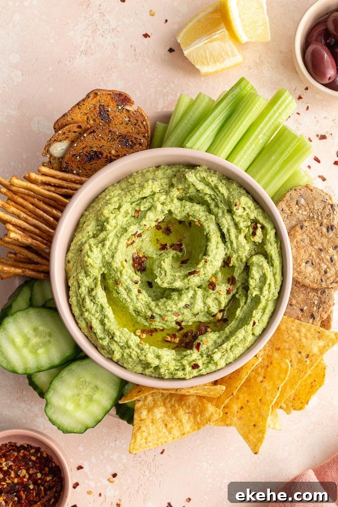 Overhead view of arugula hummus in a pink bowl and surrounded by veggies and chips.