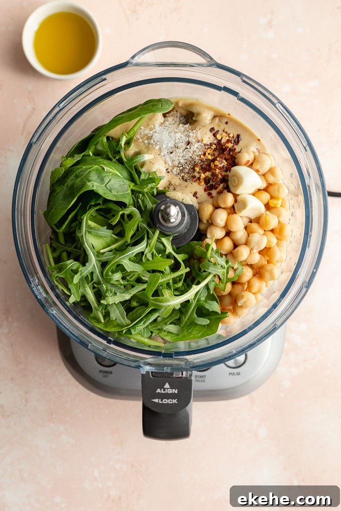 Overhead view of ingredients to make green hummus in a food processor bowl.
